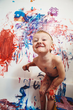Portrait of cute adorable white Caucasian little boy playing and painting with paints  on wall in bathroom having fun, lifestyle childhood concept