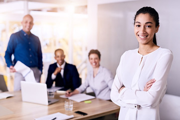 Fototapeta premium Young confident business woman standing in front of her business colleagues as all of them look happy while smiling and looking at the camera.