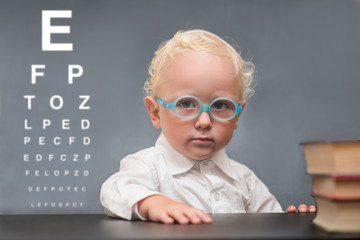Child with glasses sits at a table on the background of the table for an eye examination