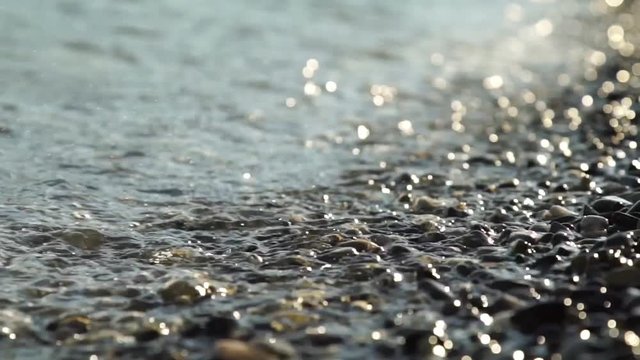 Close-up movie waves and drops lapping agains a pebble beach with shallow depth of field.