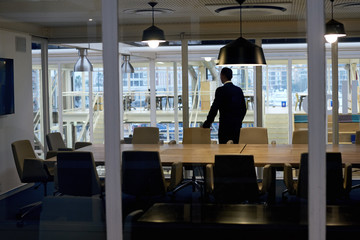 Successful business man with ambition standing alone in conference room while looking out the window thinking about several business stratergies that he might have to pursue soon.