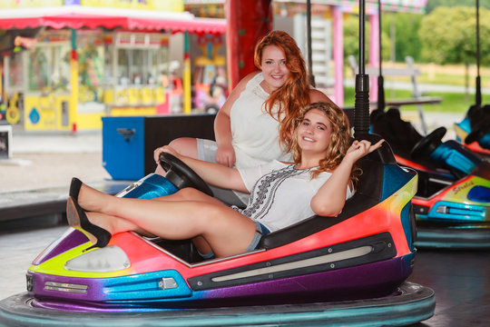 Redhead and Blonde women with large sizes have fun in the dodgems and show the peace sign