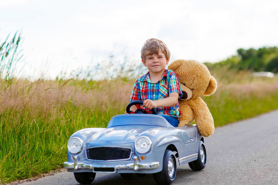 Little kid boy driving big toy car with a bear, outdoors. © Irina Schmidt
