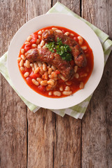Grilled sausage with beans in tomato sauce on a plate close-up. Vertical top view
