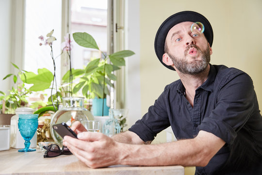 Man with hat and beard happy looking at phone and soap bubbles i