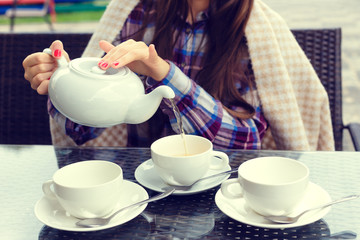 womans hands pours tea from a teapot into a cups