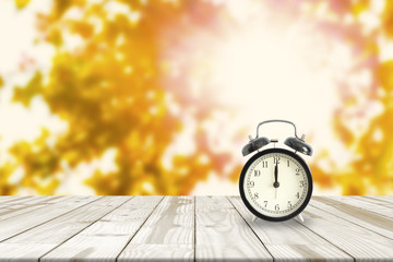 Alarm clock on Wood table and Maple leaves blurred in background