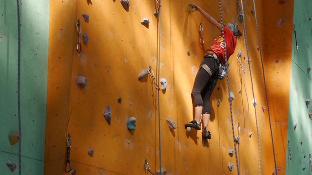 Climbing wall in the open air. Girl overcomes route with belay