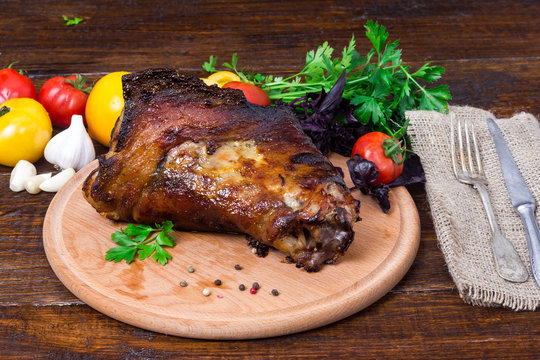fried pork leg (shin, knee wild boar) with vegetables of red and yellow tomatoes, garlic, parsley and basil on a wooden background