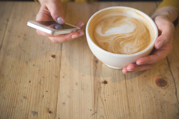 Woman with smartphone sitting in an outdoor cafe and drinking coffee. Breakfast before working day. Cappuccino and croissant on a wooden table. Girl in the cafe.
