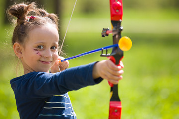 Cute girl archer with bow shooting in sunny summer day. little girl shoots bow in the park....