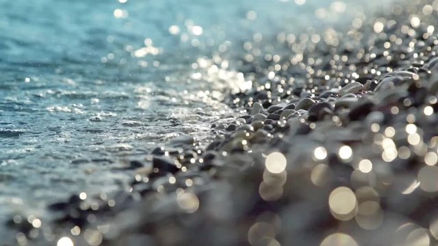 Close-up blue waves and drops lapping agains a pebble beach with shallow depth of field.