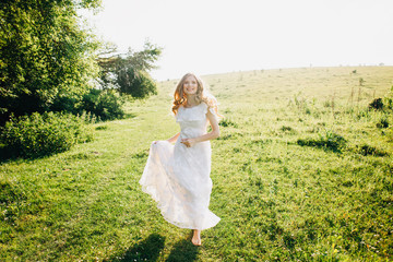Fototapeta na wymiar Young girl in a white dress in the meadow. Woman in a beautiful long dress posing in the garden. Stunning bride in a wedding dress