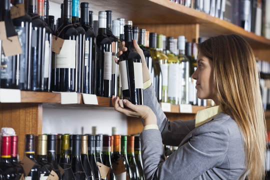 Woman Reading Wine Bottle's Label In Shop