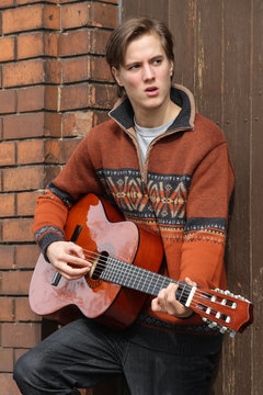 Jugendlicher singt und spielt Gitarre vor Ziegel und Holz Fassade