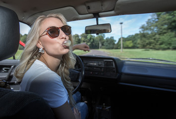 Fototapeta na wymiar Junge Frau am Steuer eines Autos kaut Kaugummi und macht eine Blase