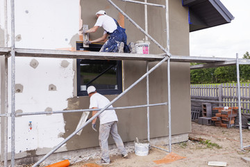 Workers spreading mortar over styrofoam insulation and mesh with trowel