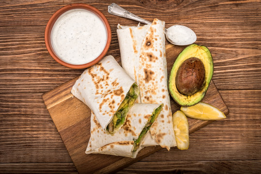 Chicken, avocado and vegetables burrito on the wooden background.