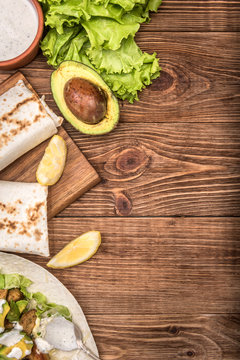 Chicken, avocado and vegetables burrito on the wooden background.