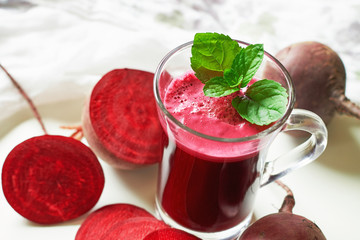Beetroot juice with mint leaves and beetroots scattered around on white background