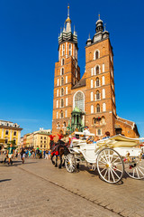 Naklejka na ściany i meble Church of St. Mary in the main Market Square with beautifully decorated horse and white old coach in the foreground. Basilica Mariacka. Krakow. Poland.