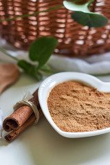 Powdered cinnamon in heart shaped bowl with cinnamon sticks next to it on white surface