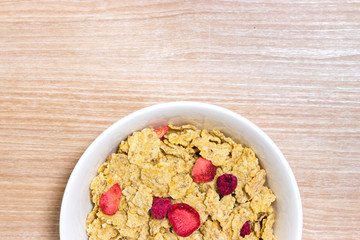 Cereal with strawberry in white bowl on wooden table
