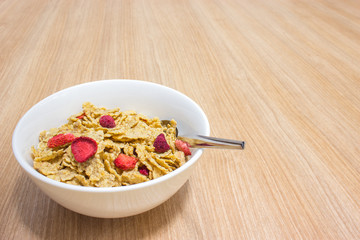 Cereal with strawberry in white bowl on wooden table