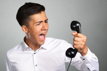 Naklejka premium An angry and irritated young man screams into the telephone receiver