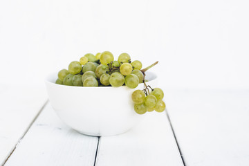 White seedless grapes in white porcelain bowl on white wooden table