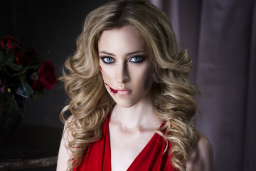 Beautiful young blonde woman in red dress with halloween make up and bloody face art