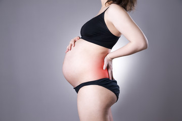 Caucasian pregnant woman in black lingerie with back pain on gray studio background