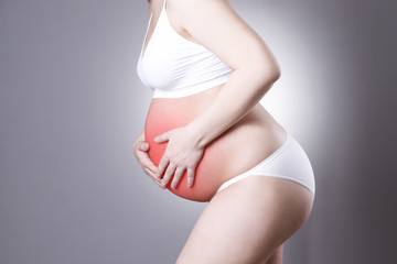 Caucasian pregnant woman in white lingerie with abdominal pain on gray studio background