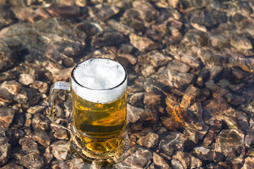 Mug fresh beer sparkles on stone in river