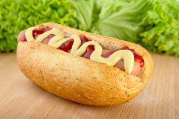 Hotdog with mustard and ketchup with lettuce in the background on wooden desk