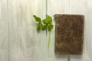 Green parsley leaves and little old book on wooden background