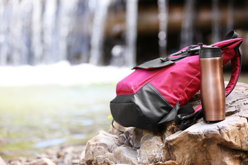 Backpack and bottle on stone on waterfall background