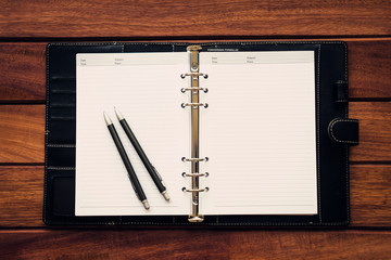 Personal organizer with pen and pencil on wooden table background, flat lay, workplace and business concept