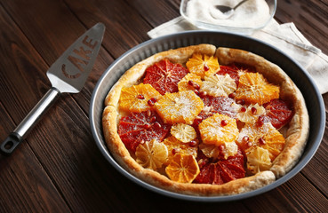 Delicious citrus cake in pan on wooden background