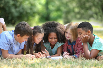 Cute kids reading book on green grass