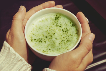 Female hands holding cup of green matcha tea closeup