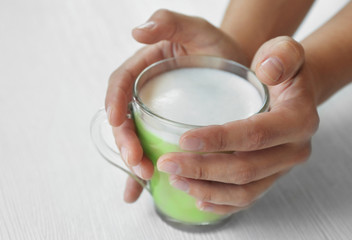 Female hands holding cup of green matcha tea on wooden background