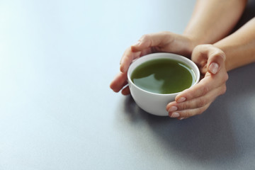 Female hands holding cup of green matcha tea on color background