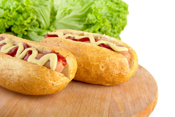 Casual hotdogs on round cutting board with salad on white