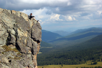 Hiker with backpack sitting on top off high rocks. Tourism conce