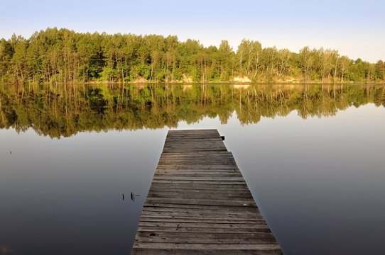 Wooden pier by the river and the forest reflected in water. © struvictory