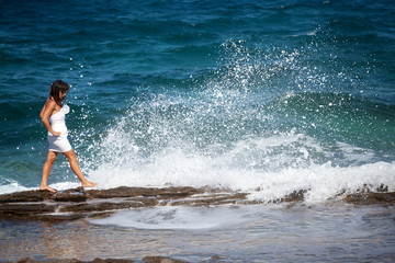 Woman in a white dress walks on the rocky beach