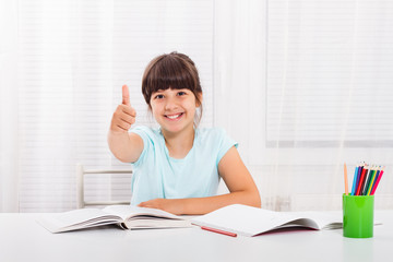 Cute little girl is showing thumbs up while she is doing her homework.