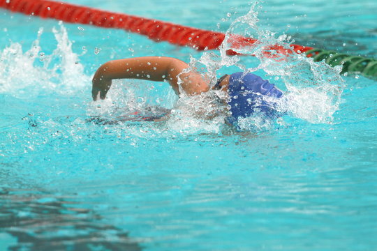 Young Asian man wearing blue cap swims freestyle stroke in a swimming pool for competition