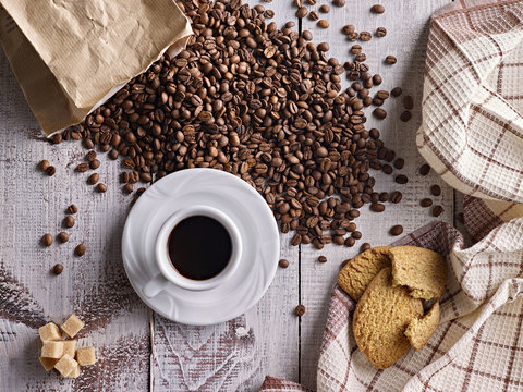 Top view on cup of coffee served with brown sugar and biscuits. Decorated with coffee beans.